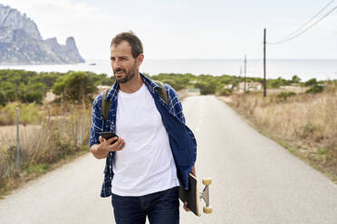 Mann mit Mobiltelefon und Skateboard auf der Straße - VEGF06028