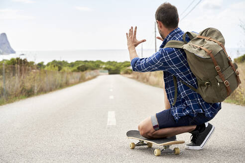 Mann mit Rucksack kniend auf Skateboard - VEGF06030