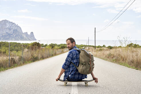 Mann mit Rucksack auf Skateboard sitzend - VEGF06033