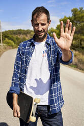 Mann mit Skateboard gestikuliert Stoppschild an einem sonnigen Tag - VEGF06051