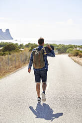 Man wearing backpack walking with skateboard on road - VEGF06054