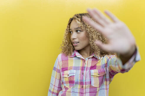 Young woman gesturing stop over yellow background - JCCMF07617