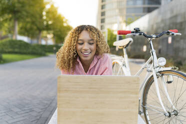 Glückliche Frau bei einem Videogespräch mit dem Laptop auf dem Fahrrad - JCCMF07644