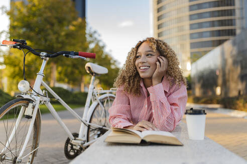 Lächelnde Frau mit Buch und Einweg-Kaffeetasse auf einer Bank liegend - JCCMF07648