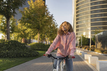 Nachdenkliche junge Frau fährt mit dem Fahrrad auf einem Fußweg in der Stadt - JCCMF07654