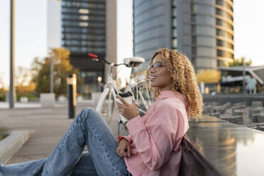 Smiling contemplative woman having coffee on footpath - JCCMF07656