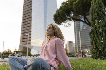 Smiling woman relaxing on grass in city - JCCMF07668