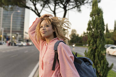 Young woman with curly blond hair carrying backpack crossing street - JCCMF07669