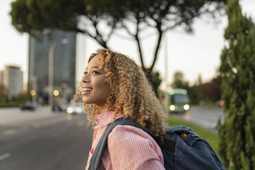 Smiling blond woman with backpack contemplating at sunset - JCCMF07671