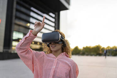 Junge Frau mit VR-Brille und erhobener Hand auf dem Fußweg - JCCMF07682