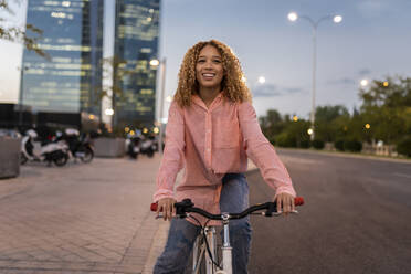 Smiling blond woman riding bicycle on road in city - JCCMF07685