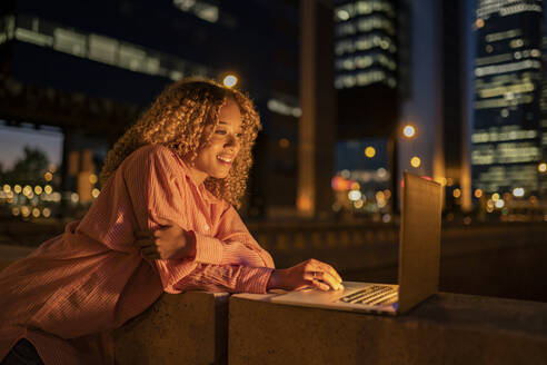 Lächelnde Frau mit Laptop an der Wand bei Nacht - JCCMF07696