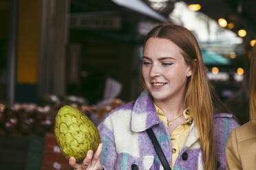 Happy woman looking at custard apple in farmer's market - ACTF00245