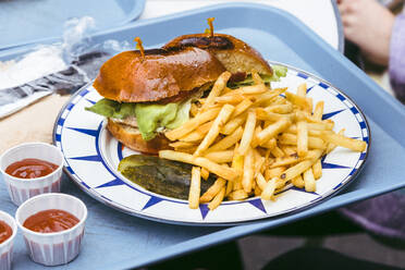 Fischsandwich mit Essiggurken und Pommes frites in einem Teller auf einem Tablett - ACTF00249