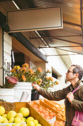 Mann mit wiederverwendbarer Tasche betrachtet Protea-Blüten auf dem Markt - ACTF00250