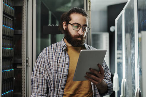 Techniker mit Brille schaut auf einen Tablet-PC im Serverraum - DSHF00578