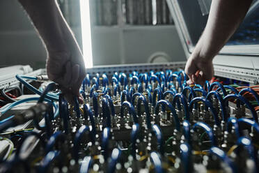 Die Hände eines Technikers, der die blauen Kabel am Netzwerkserver anschließt - DSHF00594