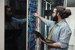 Techniker, der ein Kabel an einen Server anschließt und einen Laptop im Serverraum hält - DSHF00597