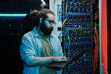 IT-Experte arbeitet an einem Laptop in der Nähe des Servers im Kontrollraum - DSHF00598