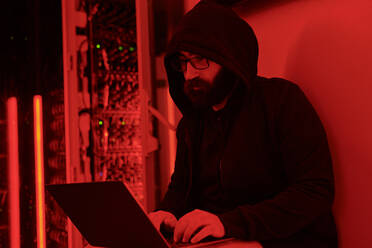 Hacker im Kapuzenpulli beim Programmieren auf einem Laptop im Serverraum - DSHF00612