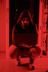 Computerhacker mit Laptop kauernd im Serverraum mit rotem Licht - DSHF00615