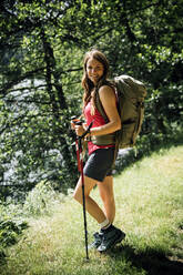 Smiling woman with hiking poles standing on grass - GIOF15560