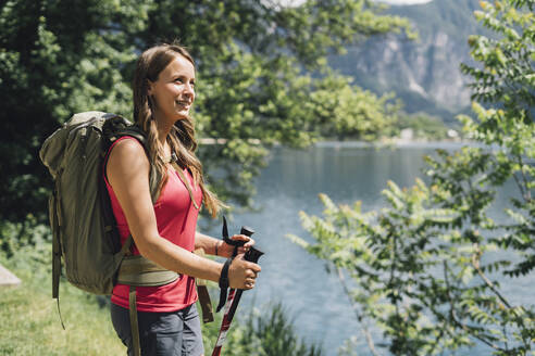 Nachdenklicher junger Wanderer mit Rucksack und Wanderstöcken - GIOF15563