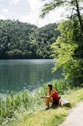 Woman spending leisure time sitting near Lake Levico on sunny day - GIOF15565