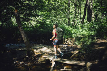 Woman exploring forest walking on tree log - GIOF15581