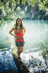 Smiling hiker walking on tree log by Lake Levico - GIOF15588