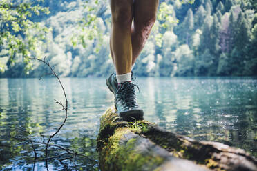 Woman wearing hiking boot walking on tree log by Lake Levico - GIOF15589