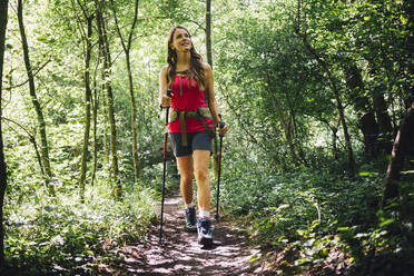 Frau erkundet den Wald mit Wanderstöcken auf einem Wanderweg - GIOF15590