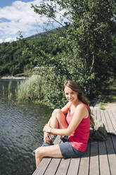 Smiling woman sitting on jetty by Lake Levico - GIOF15596