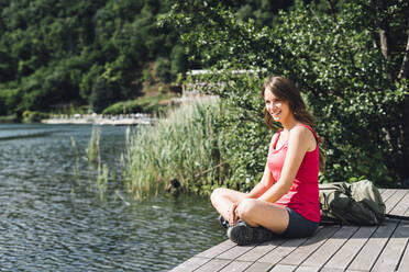 Happy hiker sitting cross-legged on jetty by Lake Levico - GIOF15597