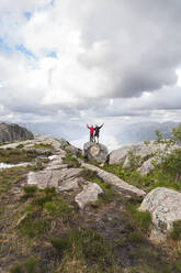 Freunde mit erhobenen Händen auf einem Felsen unter Wolken stehend - JAQF01078