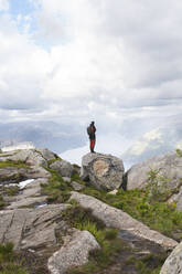 Wanderer, der auf einem Felsen stehend die Berge betrachtet - JAQF01080