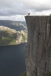 Hikers standing on edge of Pulpit rock cliff by Lysefjorden fjord, Norway - JAQF01081