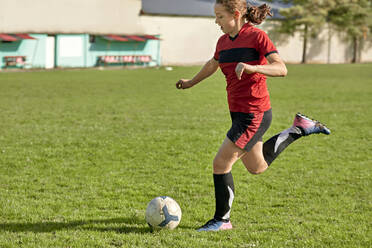 Mädchen kickt Fußball auf einem Feld an einem sonnigen Tag - ZEDF04904