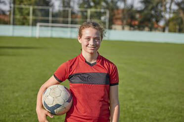 Smiling girl standing with soccer ball on sunny day - ZEDF04920