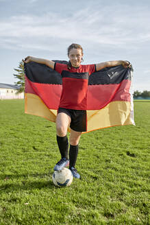 Glückliches Mädchen steht mit Fußball und hält die deutsche Flagge auf dem Feld - ZEDF04931