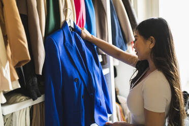 Smiling woman holding blue blazer standing in closet - DMMF00221