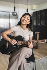 Lächelnde Frau spielt Gitarre zu Hause - DMMF00234