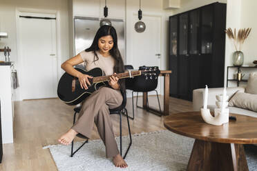 Young woman playing guitar sitting at home - DMMF00235