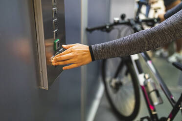 Frau drückt den Knopf eines Aufzugs mit Fahrrad - DMMF00245