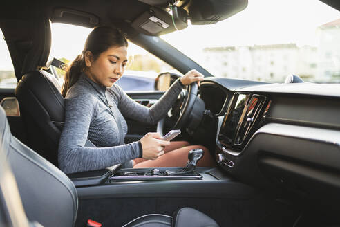 Frau benutzt Smartphone im Auto sitzend auf einer Autoreise - DMMF00253