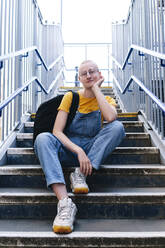 Androgyne Person mit Rucksack auf einer Treppe sitzend - ASGF02996