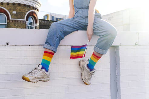 Transgender-Person mit Regenbogenfahne an der Wand sitzend - ASGF03000