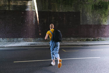 Nicht-binäre Person mit Rucksack läuft auf der Straße - ASGF03011
