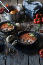 Composition of served bowls with delicious tomato creamy soup with seeds on table with tomatoes and bread buns - ADSF39552