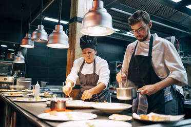 Mann und Frau in Schürzen arbeiten in einem Restaurant in der Küche und bereiten Essen für Kunden zu - ADSF39563